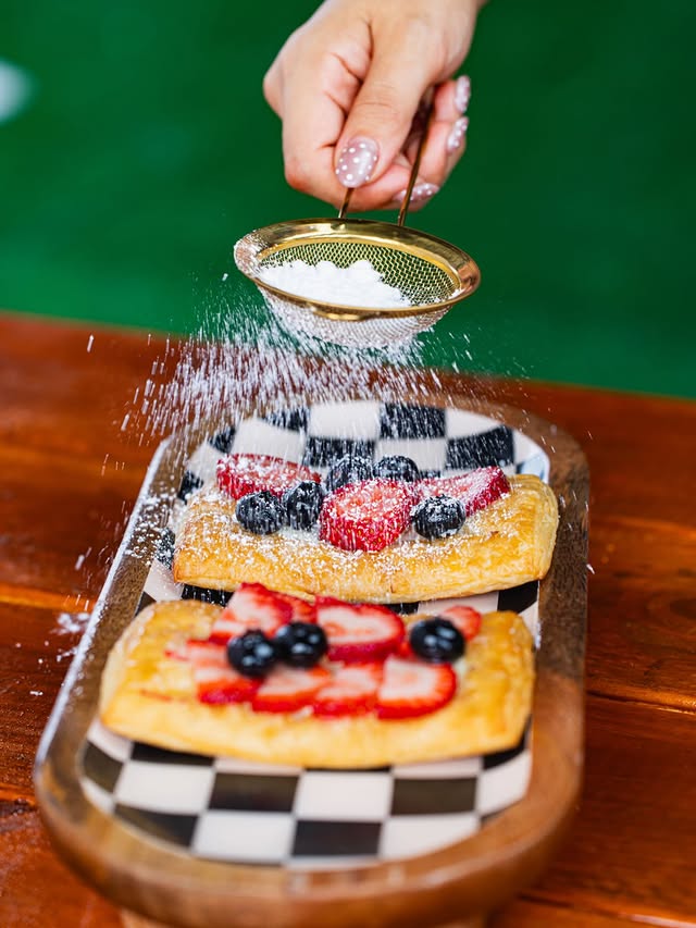 Dos pastries con fresas y arándanos mientras se espolvorea azúcar